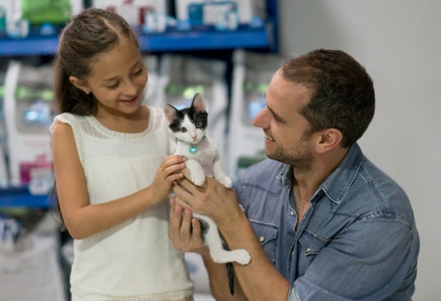 Homme qui tient dans ses mains un chaton blanc et noir qu'il montre à une petite fille